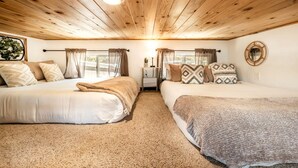 A room with two beds, a ceiling light, a window with curtains, and a wall-mounted mirror. - Beautiful Tiny Home Nestled in Woodland Park and near Manitou Springs, Perfect for a Weekend Getaway (Woodland Park)