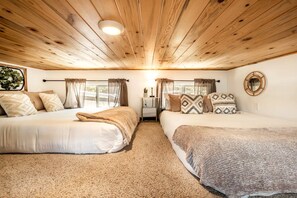 Una habitación con dos camas, una lámpara en el techo, una ventana con cortinas y un espejo instalado en la pared.