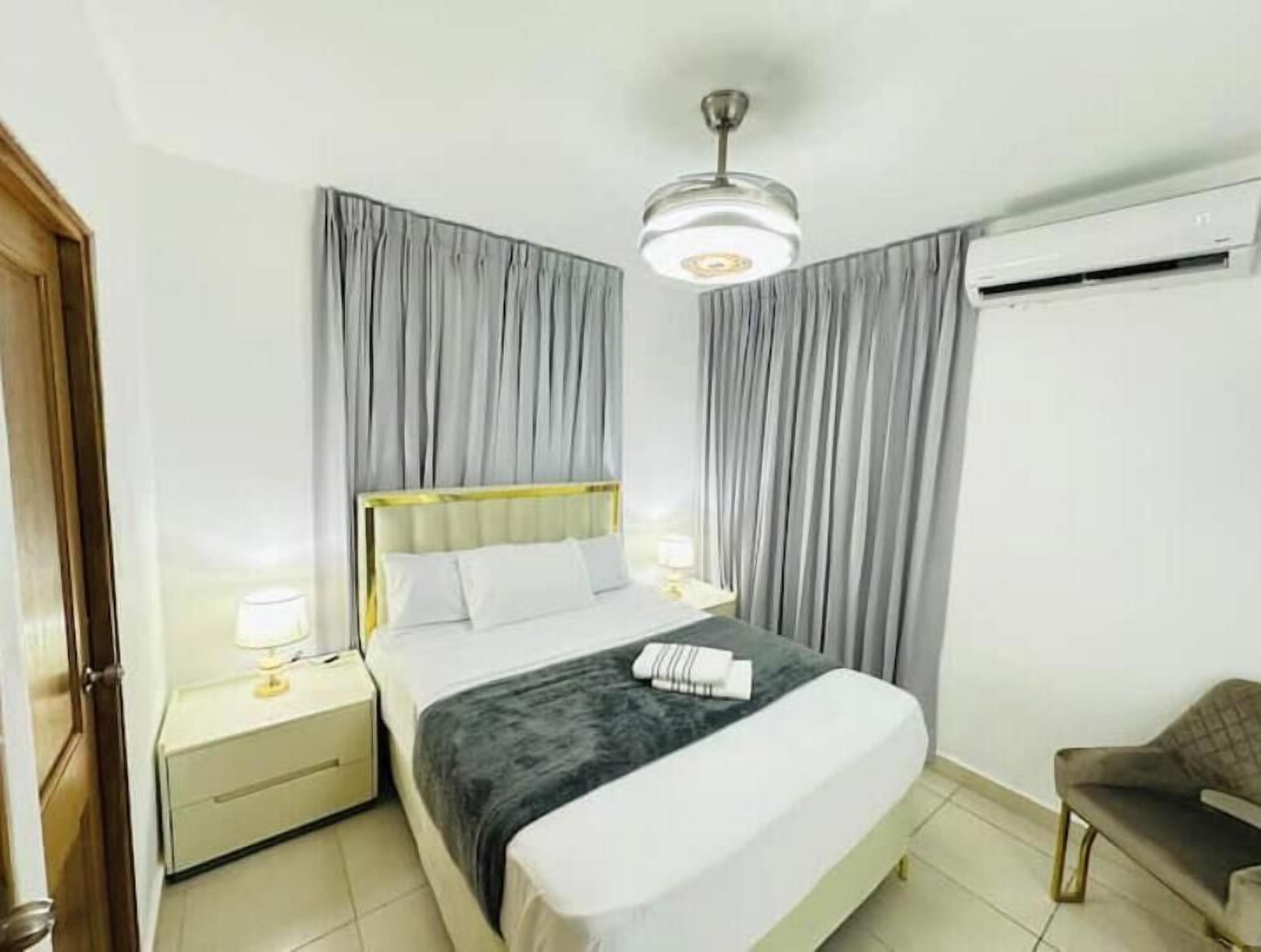 Ein Hotelzimmer mit einem Bett, einem Nachttisch, einem Sessel, einem Deckenventilator und einer Klimaanlage.