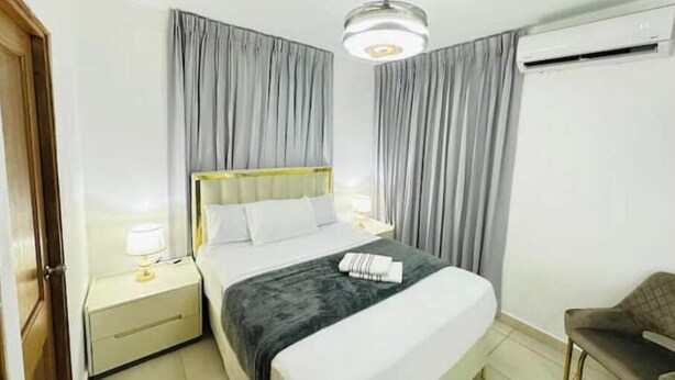 Una habitación de hotel con cama, mesita de noche, silla, ventilador de techo y aire acondicionado.