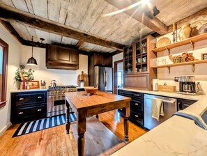 Een keuken met houten kastjes, een grote houten tafel en een hangende lamp.