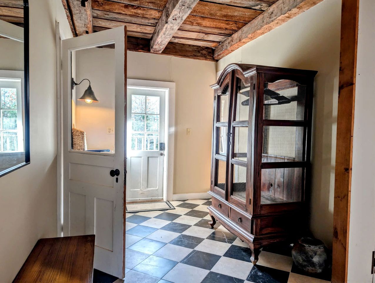 Un couloir avec un sol à carreaux, une armoire en bois et une porte dotée d’un luminaire.