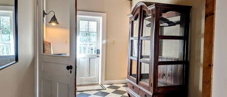 Un couloir avec un sol à carreaux, une armoire en bois et une porte dotée d’un luminaire.