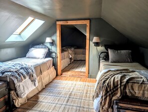 A loft bedroom with two beds, a skylight, and a wooden door leading to a lofted sleeping area. - Elegant Luxury Cottage with Fire Pit Near Carrying Place Beach in Surry, Maine (Surry)