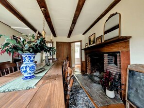 A dining area with a long wooden table, chairs, a blue and white vase, a fireplace, and a chandelier. - Elegant Luxury Cottage with Fire Pit Near Carrying Place Beach in Surry, Maine (Surry)