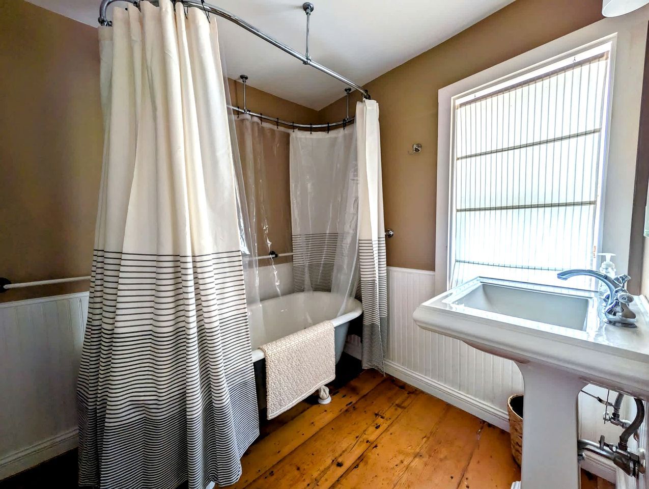 A bathroom with a bathtub, a shower, a sink, and a window with blinds.