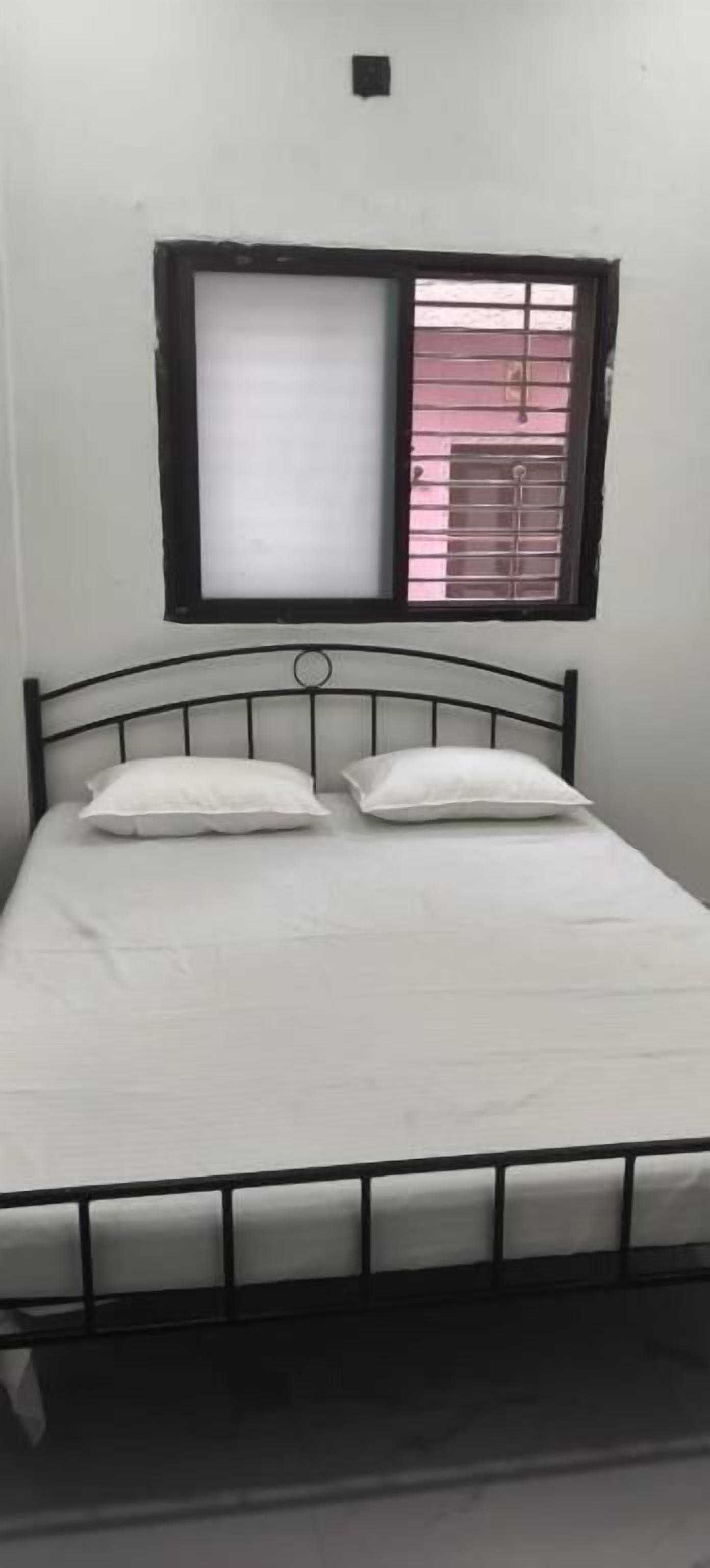 A single bed with a metal frame, white bedding, and a window with a black frame.