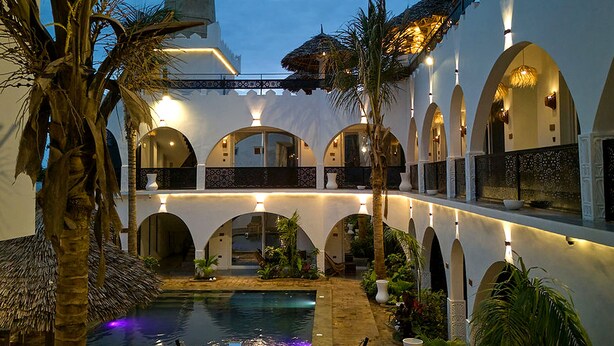 Ein Innenhof mit Pool, Palmen und bogenförmigen Gängen.