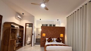 Ein Schlafzimmer mit Bett, Kleiderschrank, Deckenventilator und einem durchgehenden Türspalt sichtbaren Badezimmer.