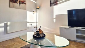 Uma sala de estar moderna com uma mesa de centro de vidro, uma televisão de tela plana e obras de arte nas paredes.