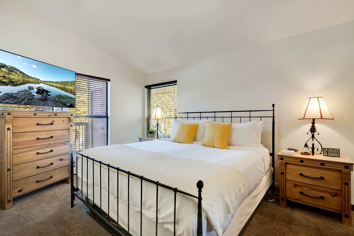 Un dormitorio con cama, cómoda de madera, mesitas de noche y un ventanal con vista a un lago.