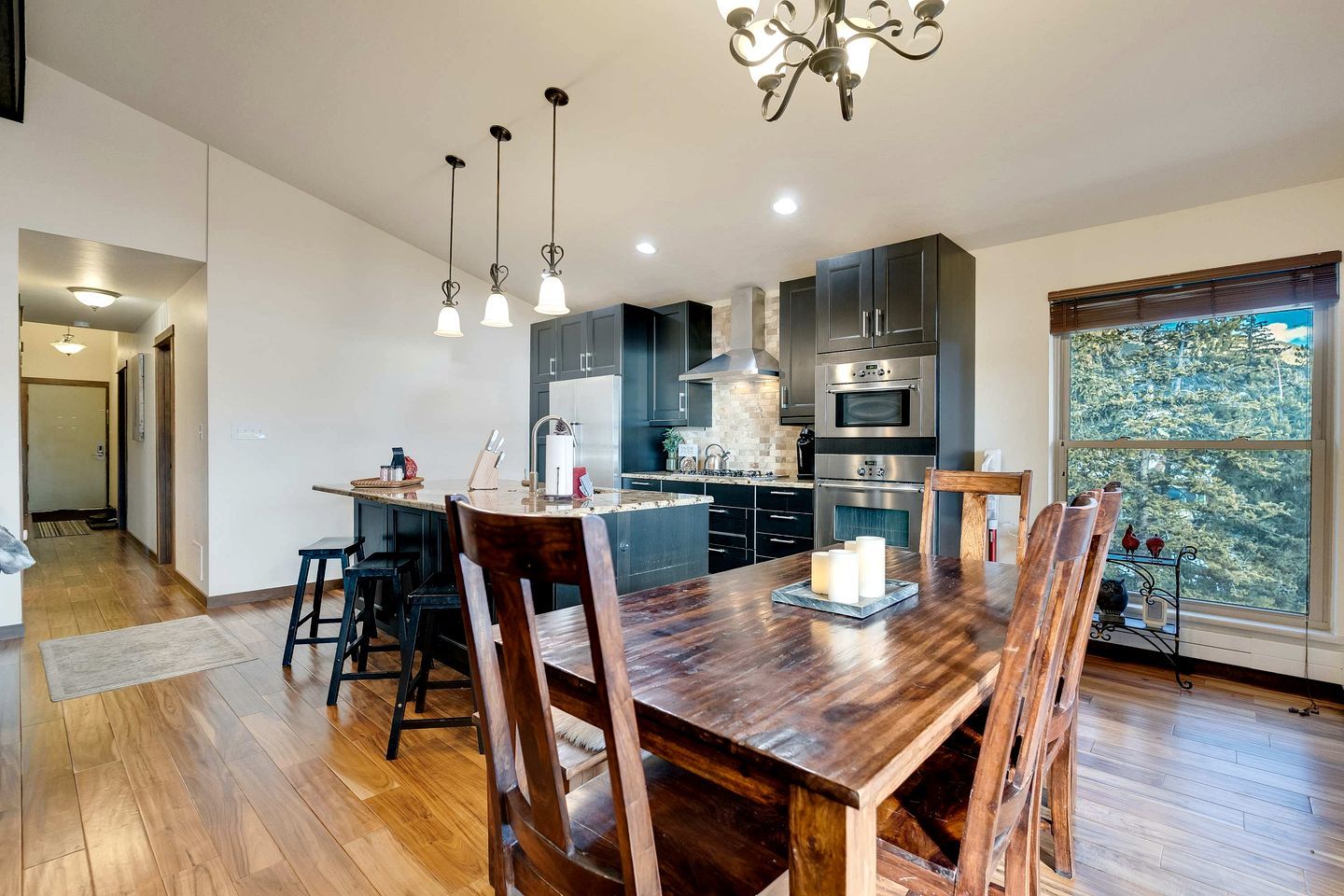 Una cocina moderna con armarios oscuros, electrodomésticos de acero inoxidable y una mesa de comedor de madera con sillas.