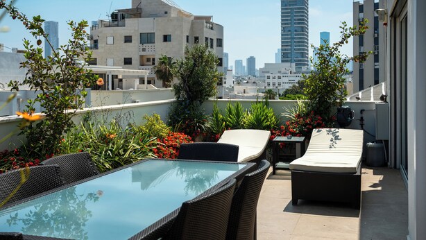 Eine Dachterrasse mit Glastisch, Korbstühlen und einer Liege.