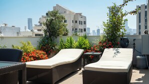 Eine Dachterrasse mit zwei Liegestühlen, einem Tisch und unterschiedlichen Pflanzen.