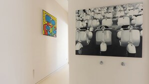 Eine Wand mit zwei Kunstwerken; eines ist ein farbenfrohes abstraktes Werk, das andere ein monochromatisches Foto einer Reihe klassischer Autos.