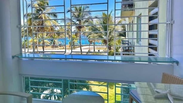 A room with a large window overlooking a pool and palm trees. - Elegant apartment with a view of the ocean (Santo Domingo Este)