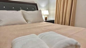 A neatly made bed with a beige bedspread and two rolled white towels placed on the bed. - Elegant apartment with a view of the ocean (Santo Domingo Este)