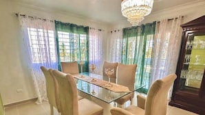A dining area with a glass table surrounded by cushioned chairs, a chandelier, and curtains. - Elegant apartment with a view of the ocean (Santo Domingo Este)
