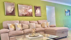 A living room with a beige sofa, a glass coffee table, and three framed artworks on the wall. - Elegant apartment with a view of the ocean (Santo Domingo Este)