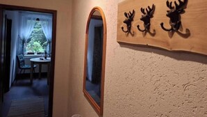 A hallway with a mirror, a wooden sign with animal head hooks, and a view into a room with a table and chairs. - Ulbersdorf Mill "Försterstübchen" (Hohnstein)