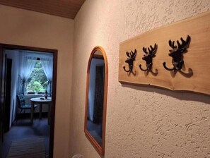 Ein Korridor mit Spiegel, einem Holunderschild mit Aufhängungen in Tierform und Blick in einen Raum mit Tisch und Stühlen.