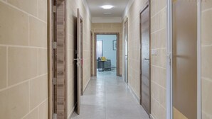 Een gang met beige betegelde muren en deuren, die leidt naar een kamer met een bed en een raam.