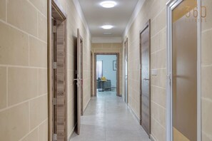 A hallway with beige tiled walls and doors, leading to a room with a bed and a window. - A 3BR equipped home w/WIFI Next to St Thomas Bay (Marsaskala)