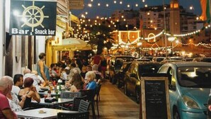 Een levendig buitengebied met eettafels en stoelen, sfeerverlichting erboven en een bord voor een bar en snackbar.