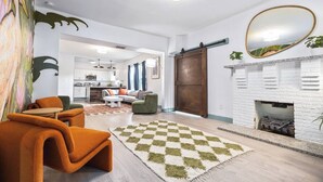 Uma sala de estar moderna com lareira, um tapete xadrez e um espaço de jantar com cadeiras laranja.