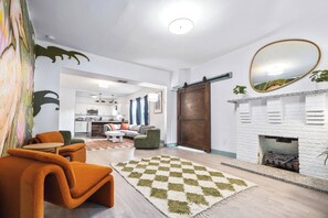 Ein modernes Wohnzimmer mit Kamin, einem Schachbrettteppich und einem Essbereich mit orangefarbenen Stühlen.