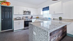 Uma cozinha moderna com armários brancos, bancada de granito, eletrodomésticos de aço inoxidável e uma parede de destaque em madeira.