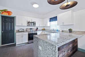 Eine moderne Küche mit weißen Schränken, einer Arbeitsplatte aus Granit, Edelstahlgeräten und einer Wand mit Holzakzenten.