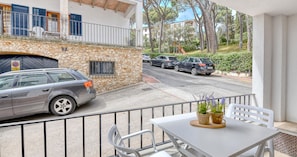 Ein Balkon mit Tisch und Stühlen, eine Steinsäule und parkende Autos auf der Straße.