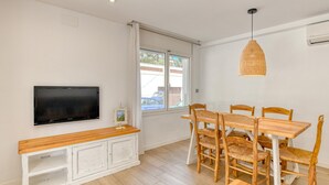 A dining area with a TV, wooden dining table, wicker chairs, and a pendant light. - Renovated ground-floor apartment in the center of Calella de Palafrugell (Calella de Palafrugell)