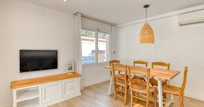 Ein Essbereich mit Fernseher, einem Holztisch, Korbstühlen und einer Pendelleuchte.