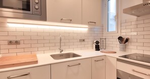 Eine moderne Küche mit weißen Schränken, einer Edelstahl-Spüle, einer Mikrowelle und einem Fenster.