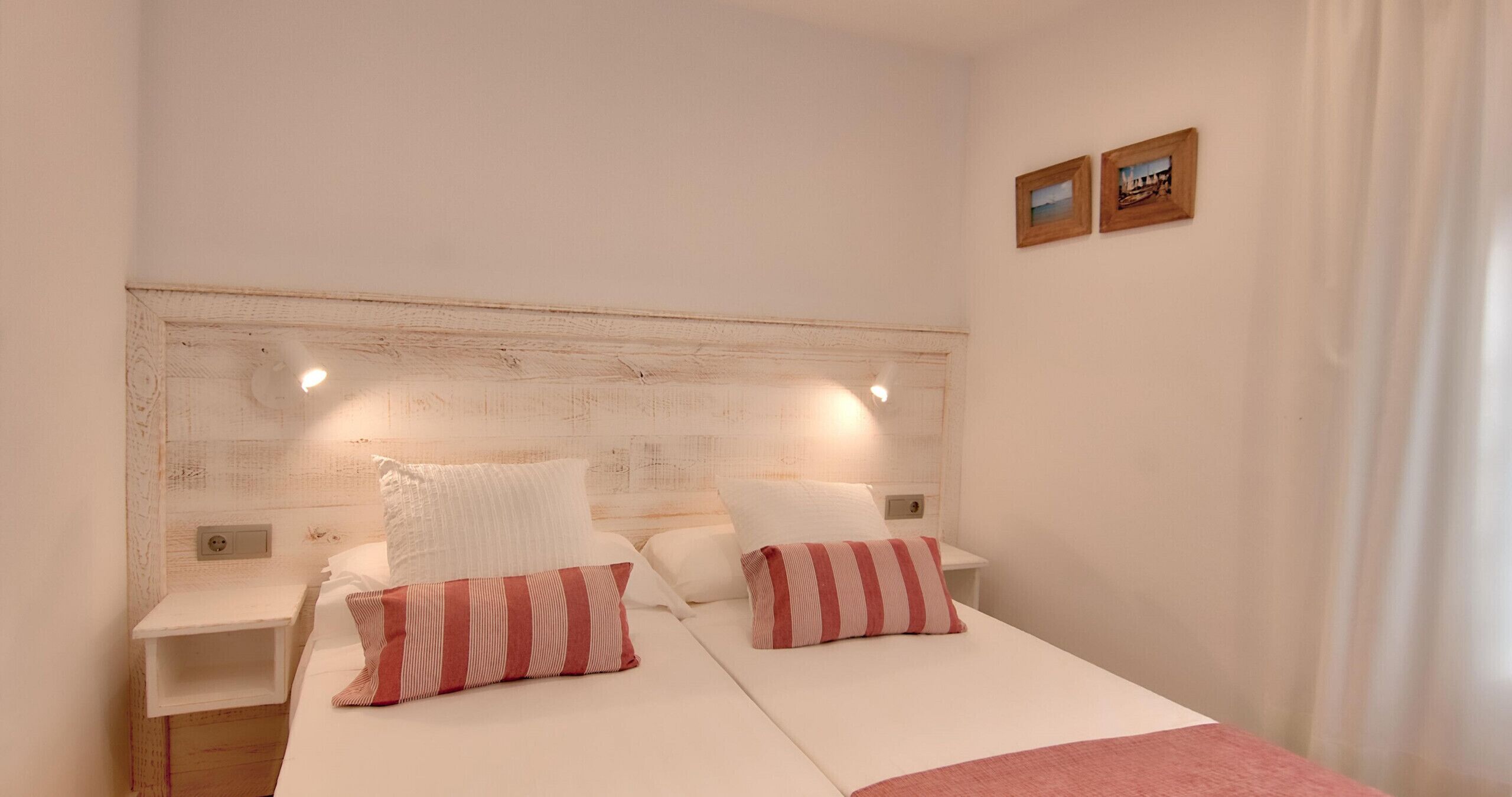 A double bed with white bedding and striped pillows, a wooden headboard, bedside tables, and two framed pictures on the wall.