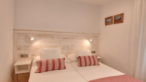 A double bed with white bedding and striped pillows, a wooden headboard, bedside tables, and two framed pictures on the wall. - Renovated ground-floor apartment in the center of Calella de Palafrugell (Calella de Palafrugell)
