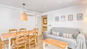 A living room with a grey sofa, wooden dining table, wicker chairs, a hanging light fixture, and framed artwork on the wall. - Renovated ground-floor apartment in the center of Calella de Palafrugell (Calella de Palafrugell)