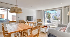 A modern living room with a wooden dining table, wicker chairs, a grey sofa, and a TV on the wall. - Ground-floor apartment with a spacious terrace in the center of Calella de Palafrugell (Calella de Palafrugell)