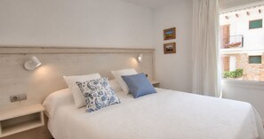 A bedroom with a bed, two bedside tables, a headboard, and a window with a view of buildings. - Ground-floor apartment with a spacious terrace in the center of Calella de Palafrugell (Calella de Palafrugell)
