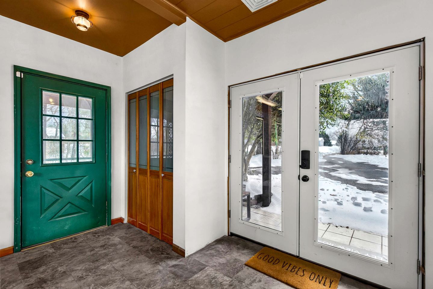 A front entryway with a green door, a wooden door, and a glass door with a view of a snowy landscape.