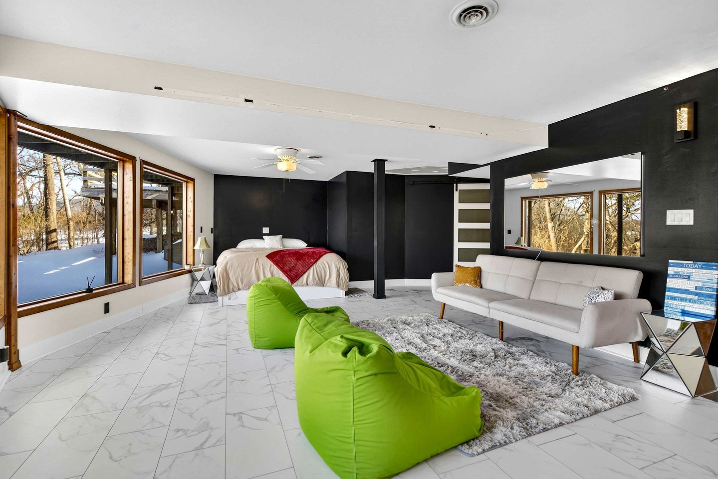 A modern living room with a large bed, a sofa, and green bean bags.