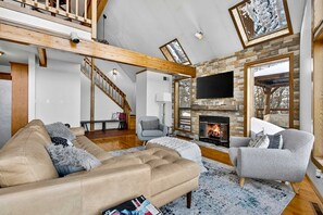 Un amplio salón con chimenea, un televisor grande y un techo alto con vigas a la vista.