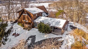 Eine Holzhütte mit schneebedecktem Dach, umgeben von Bäumen und einer verschneiten Landschaft.