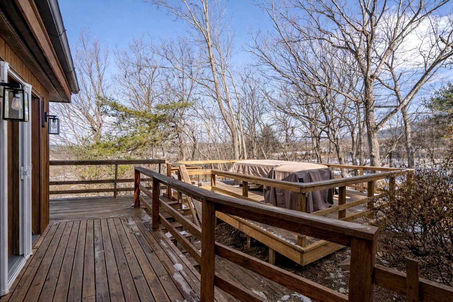 Une terrasse en bois dotée d’un espace salon abrité et offrant une vue sur des arbres sans feuilles.