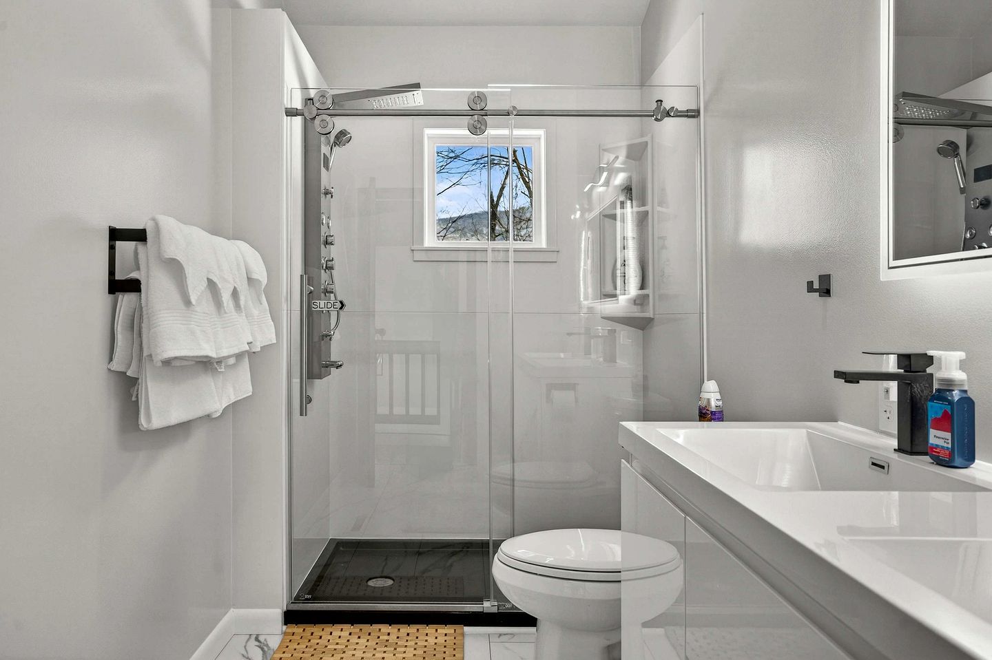 Et moderne badeværelse med et glasafskærmet brusebad, toilet og håndvask med toiletartikler.