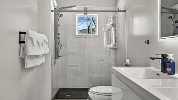Et moderne badeværelse med et glasafskærmet brusebad, toilet og håndvask med toiletartikler.