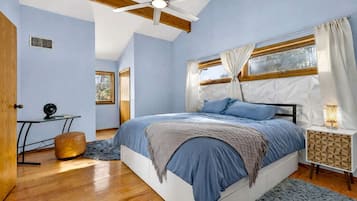 A bedroom with a bed, a desk, a chair, a window, and a ceiling fan.