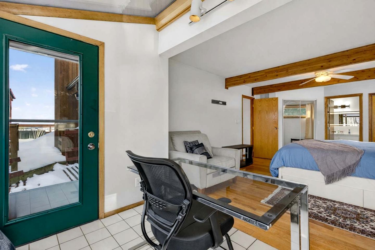 Une pièce avec une table en verre, un canapé blanc, un plafond en bois et une porte donnant sur l’extérieur.